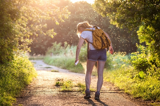 Woman with backpack applying insect repellent agains mosquito and tick outdoors